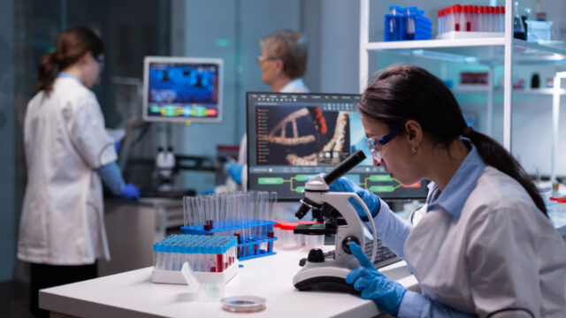 Biochemist scientists studying reaction of virus on microscope in laboratory