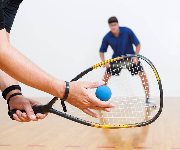 Two men playing racquetball on court. One serving.